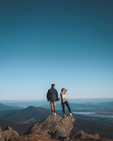 Van life influencers Harry and Jordan posing on a rock edge, with mountains in the background