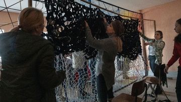 Women and teens in Solotvyno, Ukraine, knotting military camouflage nets that will be sent to the front lines.