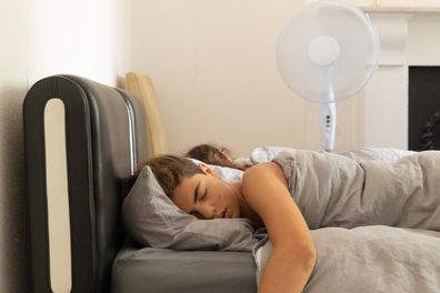 A boy and a girl sleep refreshed by a fan on black leather bed. Copy space