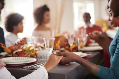 Young woman and her daughter holding hands and saying grace with their multi generation family at the Thanksgiving dinner table, detail, focus on foreground.