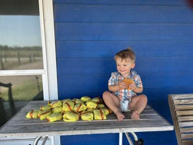 Toddler sitting next to a pile of cheeseburgers.