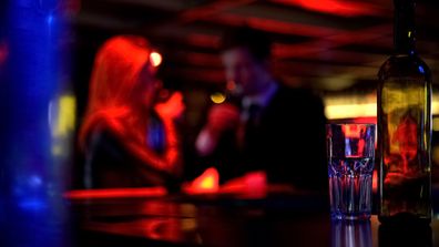 Man and woman meeting in nightclub, both having drinks, blurred background
