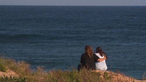 Grande plano de duas pessoas se abraçando em uma praia. 