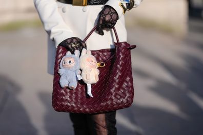 A guest wears a burgundy bordeaux woven Bottega Veneta Andiamo leather bag, light blue Labubu bag charm, cream Labubu bag charm, outside Elie Saab, during the Paris Fashion week Women's Fall/Winter 2025-2026 on March 8, 2025 in Paris, France.