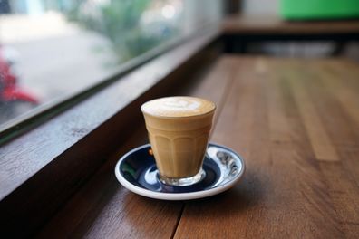 Hot Piccolo Latte - A glass of coffee with milk and beautiful leaf pattern latte art on wooden table and copy space, Perfect for breakfast time.