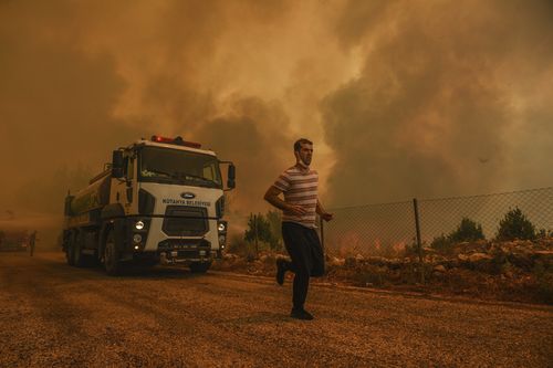 A man runs, in the fire-devastating Sirtkoy village, near Manavgat, Antalya, Turkey, Sunday, Aug. 1, 2021. (AP Photo)