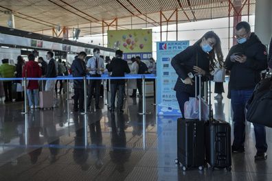 A couple fill in their health declaration via a smartphone as travelers with luggage line up at the Air Macao flight check in counter at the Beijing Capital International Airport in Beijing on Dec. 29, 2022. Gambling haven Macaos relaxation of border restrictions after China rolled back its "zero-COVID" strategy is widely expected to boost its tourism-driven economy. (AP Photo/Andy Wong)