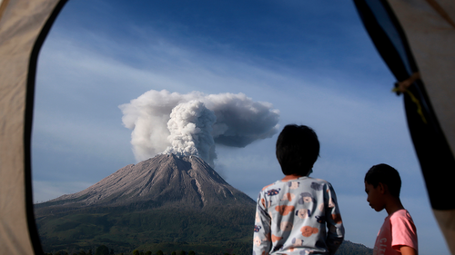 Indonesian youths are seen from the opening of a tent as they watch Mount Sinabung erupting in Karo, North Sumatra, Indonesia, Thursday, March 11, 2021. (AP Photo/Binsar Bakkara)