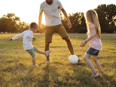 Kids and father playing soccer on a beautiful summer afternoon outdoors