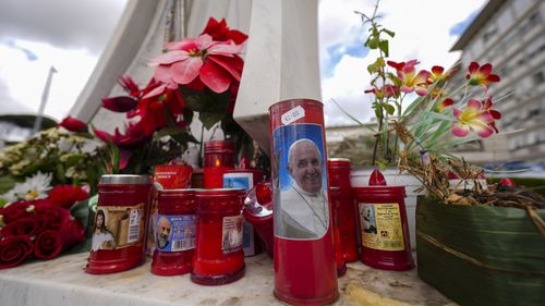 Candles, one showing a photo of Pope Francis, are seen in front of the Agostino Gemelli Polyclinic in Rome, Friday, Feb. 14, 2025, where Pope Francis has been hospitalized to undergo some necessary diagnostic tests and to continue his ongoing treatment for bronchitis. (AP Photo/Andrew Medichini)