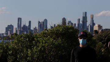 A man wears a face mask as he walks through Elwood Beach in Melbourne.