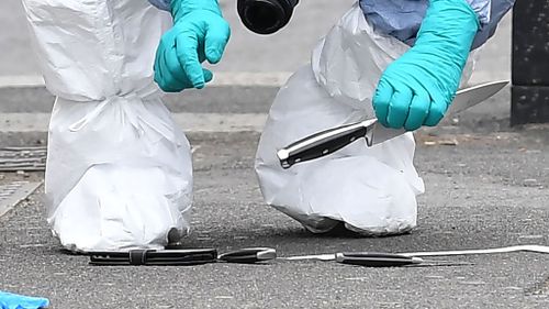 Forensic officers look at the knives found at the scene. (AFP)