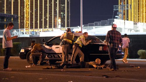 Police crouch behind a patrol car with their weapons trained on the casino. (Getty)
