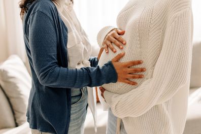 Woman touching pregnant surrogate mum's belly.