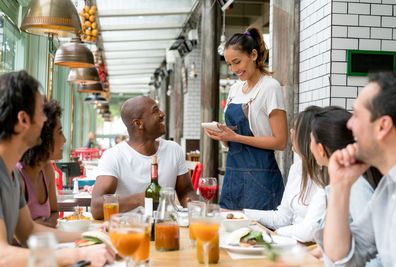 Happy waitress taking orders to a group of people eating together at a restaurant