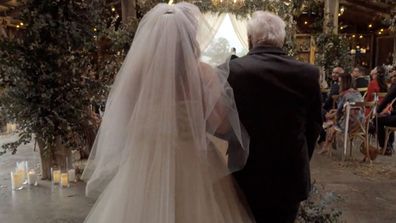 A bride is being walked to meet her groom by her father.