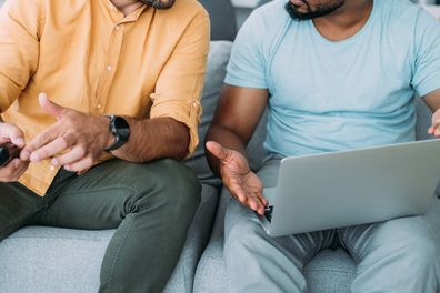 Shot of two young friends  using laptop for online betting while watching football match on the television.