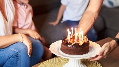 Shot of a man bringing a birthday cake for his wife with kids sitting by