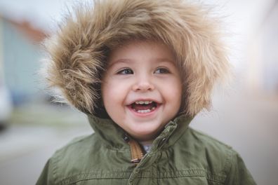 Beautiful 2 year old baby girl is smiling happily. A close up photo of her face full of joy and happiness. It's winter time, so she is wearing fury hoodie around her head.