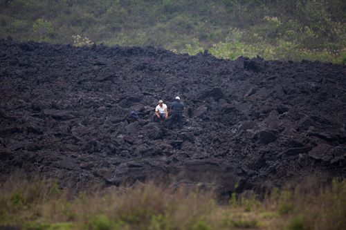 Men chat amid a band of hardened lava that flowed from the Pacaya Volcano, near El Patrocinio village in San Vicente Pacaya.
