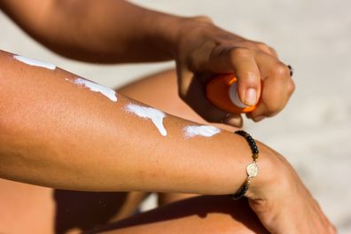 Close up on woman applying sun cream on her arm with a spray at the beach on a warm, sunny day. Sunscreen protection, skin cancer concept