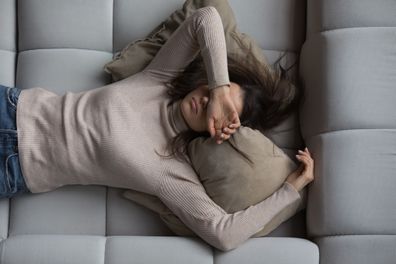 Woman lying on her couch at home, covering her eyes with hand