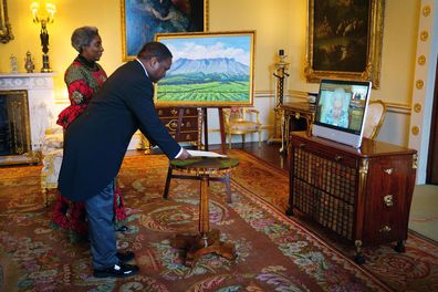 Queen Elizabeth II appears on a screen via videolink from Windsor Castle, where she is in residence, during a virtual audience to receive the High Commissioner of Malawi, Dr. Thomas Bisika (centre), and Mrs Bisika (left), at Buckingham Palace on March 3, 2022 in London, England. The painting in the background was a gift from the High Commissioner. 