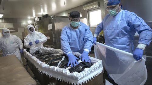 Members of the medical staff place the body of a COVID-19 victim in a coffin together with funeral house employees at the University Emergency Hospital morgue in Bucharest, Romania. 