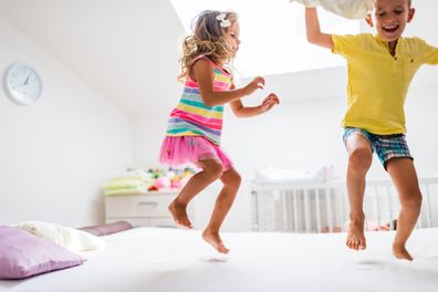 Two kids, a boy and a girl are jumping on the bed.