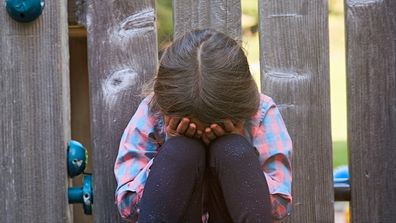 Little girl sitting outside crying with her face in her hands.