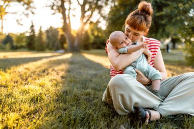 Mother and baby embracing while sitting down in meadow in sunset.