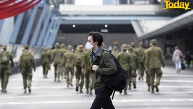 A man wearing a face mask walks past as the Australian Defence Force walk through the city.