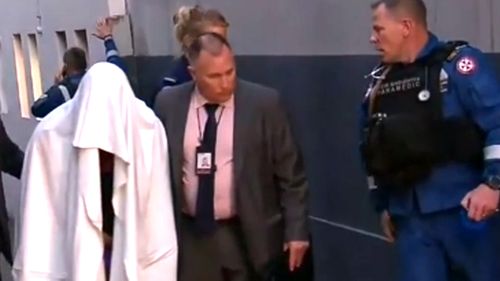 One of the men arrested in the terror raids covers himself with a blanket as he is taken away by authorities. (9NEWS)