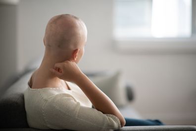 A woman is indoors in her living room. Her head is shaved due to hair loss alopecia