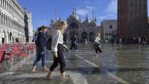 People walk in a flooded St. Mark's Square in Venice, Italy, Friday, Nov. 5, 2021. After Venice suffered the second-worst flood in its history in November 2019, it was inundated with four more exceptional tides within six weeks, shocking Venetians and triggering fears about the worsening impact of climate change.