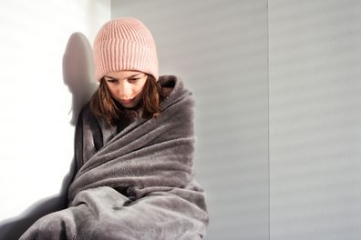 Sad young girl alone, wrapped in a blanket.