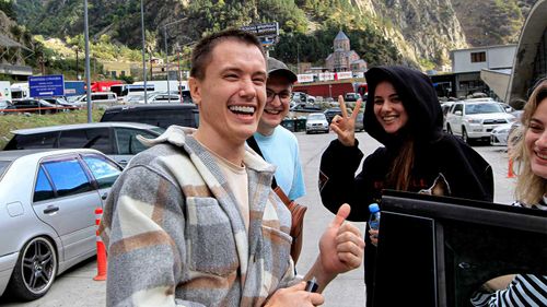 Young Russians grinning at the camera after crossing the border into Georgia rather than be drafted into the military.