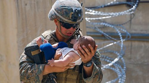 A US Marine assigned to 24th Marine Expeditionary Unit comforts an infant while they wait for the mother during an evacuation at Hamid Karzai International Airport in Kabul.