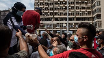 People wait to receive food and masks from the back of an aid truck on August 13, 2020 in Beirut, Lebanon
