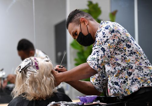 Hairdresser colours a customer's hair wearing a face mask. 