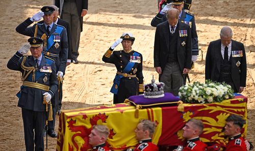 Britain's King Charles III, Britain's Prince William, Prince of Wales and Britain's Princess Anne, Princess Royal salute, alongside Britain's Prince William, Prince of Wales and Britain's Prince Andrew, Duke of York as the coffin of Queen Elizabeth II, adorned with a Royal Standard and the Imperial State Crown, arrives at the Palace of Westminster, following a procession from Buckingham Palace, in London on September 14, 2022. - Queen Elizabeth II will lie in state in Westminster Hall inside the
