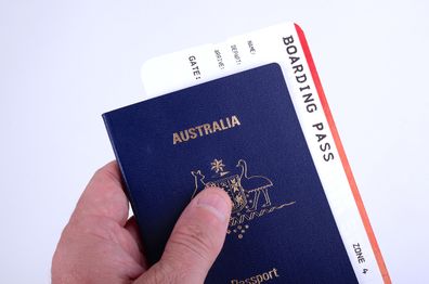 A man holds a new Australian passport with a boarding pass inserted inside the document