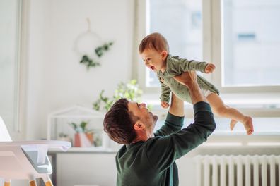 Father carrying baby son and they playing around in living room