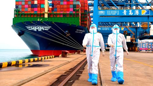 Ofițeri de inspecție a imigrației din China, îmbrăcați cu îmbrăcăminte de protecție, merg lângă o navă container într-un port din Qingdao, în provincia Shandong din estul Chinei.