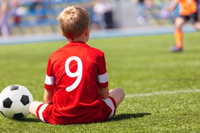 Young boy sitting on sidelines during soccer game.