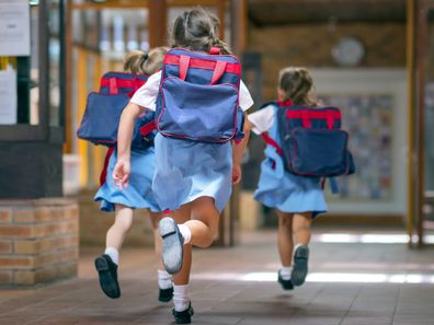 Rear view of excited students running towards entrance. Girls are carrying backpacks while leaving from school. Happy friends are wearing school uniforms.