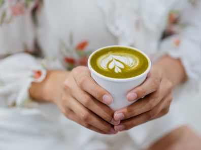 An Asian Chinese woman holding a cup of matcha latte in a cafe and ready to drink.