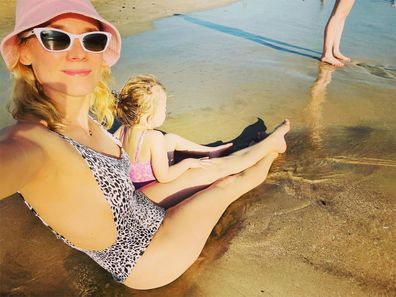 Diane Kruger taking a self wit her daughter at the beach. Her daughter's back is turned away from the camera as she sits on Diane's lap.