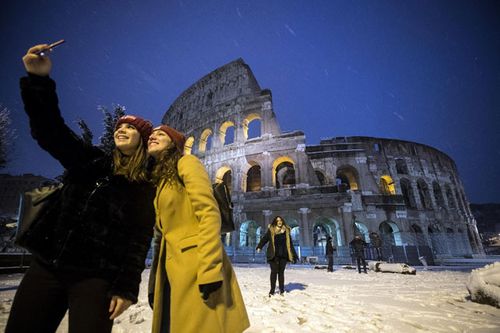 People take photographs in front of the Colosseum in Rome after historic snowfall. (AAP)