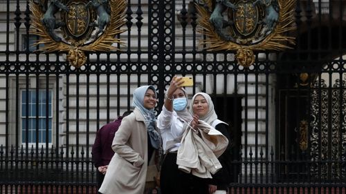 Tourists pose for selfies in front of the gates of Buckingham Palace in London. 